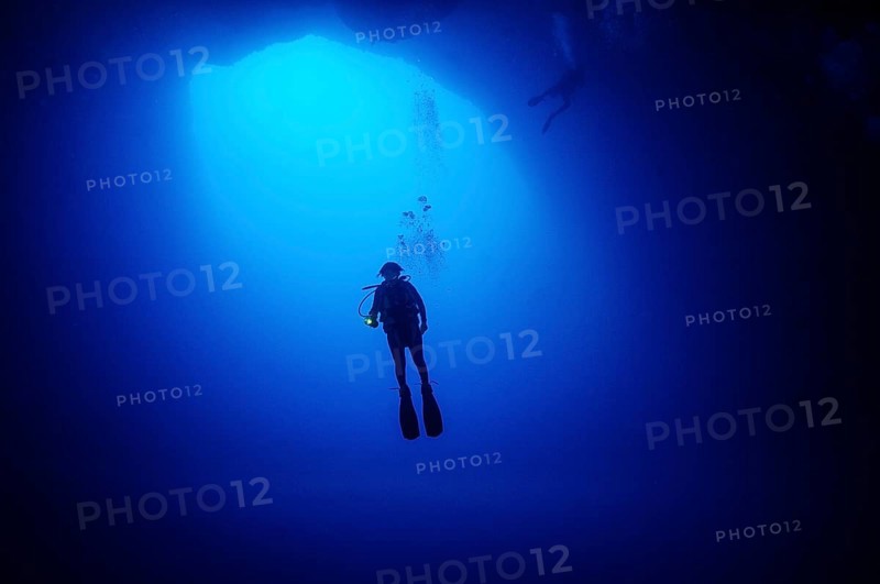Female diver scuba diver diving in floating under opening cave opening large hole in seabed entrance of vertical underwater cave cavity in coral reef collapsed karst cave Blue Hole of Nassau mt blue light in blue water, Caribbean, New Providence, Bahamas, Central America