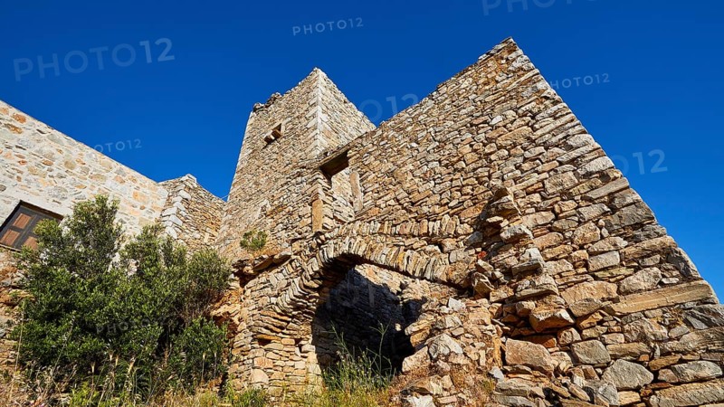 Weathered stone wall of a fortress with arches and surrounding vegetation, Vathia, residential towers village, Mani peninsula, Peloponnese, Greece, Europe