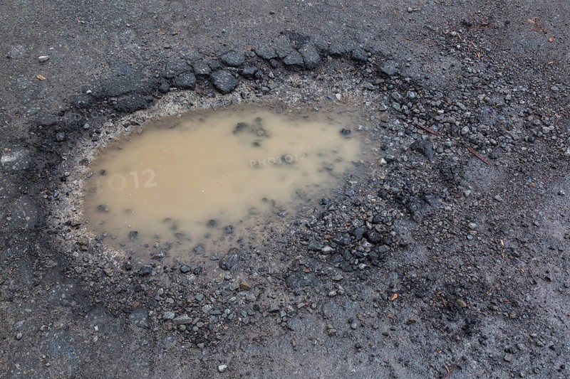 Pothole filled with rainwater on wet black asphalt road surface in spring, Montreal, Quebec, Canada, North America