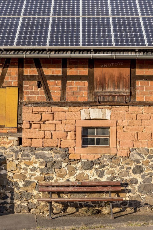 Historic farmhouse with photovoltaic system, solar panels on the roof, house wall with differently pieced masonry made of brick, sandstone, fieldstone and half-timbering, bench in front, Nidda, Hesse, Germany, Europe