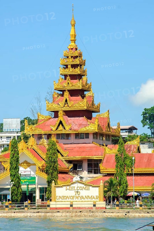 Gold and white wall with welcome greeting Welcome to Union of Myanmar on the shore of the border town Kawthaung, behind it large pagoda with golden roofs, Kawthaung, Myanmar, Asia