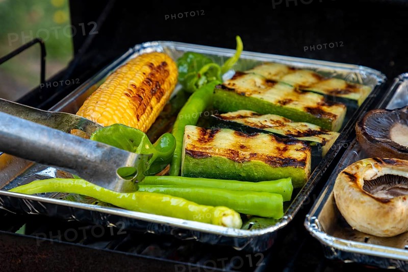 Grilled vegetables consisting of sweetcorn, green peppers and courgettes on a grill with grill tongs