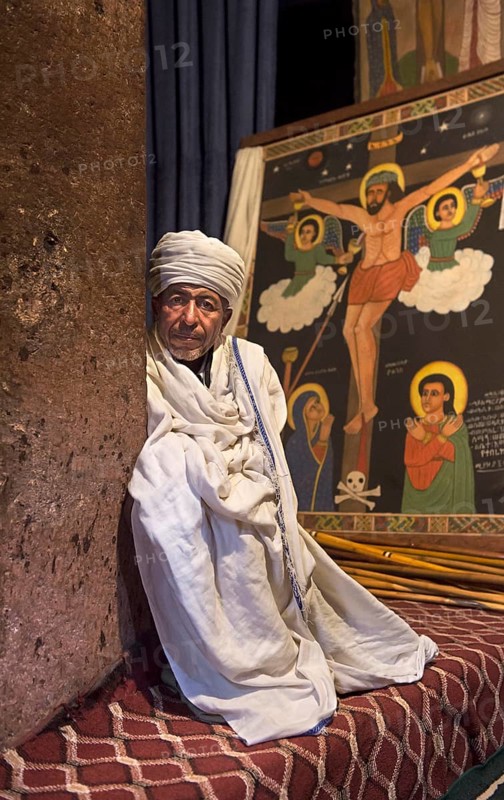 Ethiopian Orthodox priest in front of an image of the crucifixion of Jesus in the rock church of Biete Amanuel, Lalibela, Ethiopia, Africa