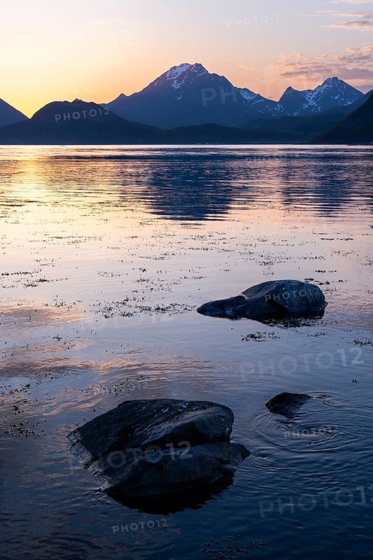 Landscape on the Lofoten Islands. View from Flakstadoya to Vestvagoya, with the snow-covered Himmeltindan mountain in the centre. The mountains are reflected in the sea. At night at the time of the midnight sun in good weather. Early summer. Lofoten, Norway, Europe