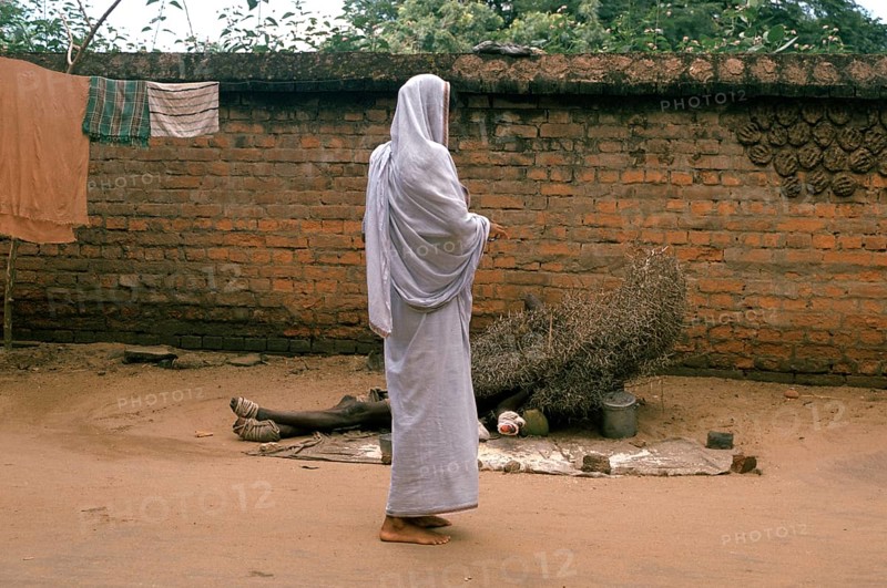 A hindu widow is giving alms to a leper (Puri, India) . The man is lying on the ground under a pile of thorny branches