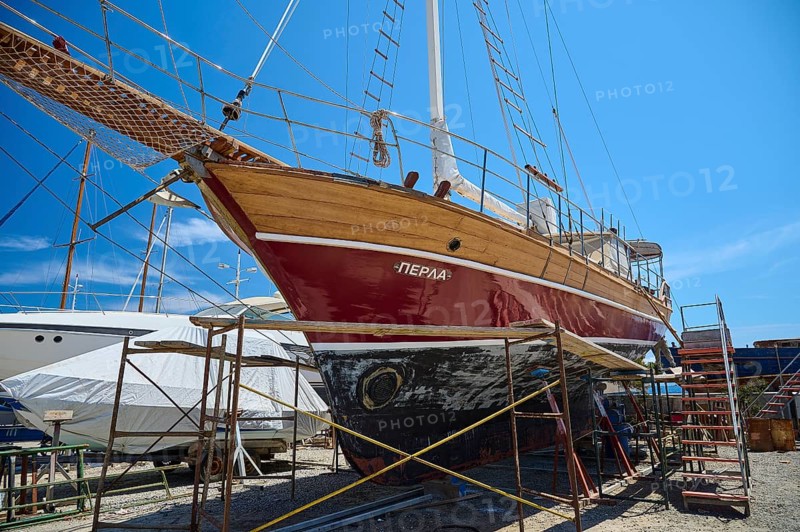 A large wooden sailing ship in dry dock with red paint and blue sky in the background, Patmos Marine, boatyard, Diakofti, Patmos, Dodecanese, Greek Islands, Greece, Europe