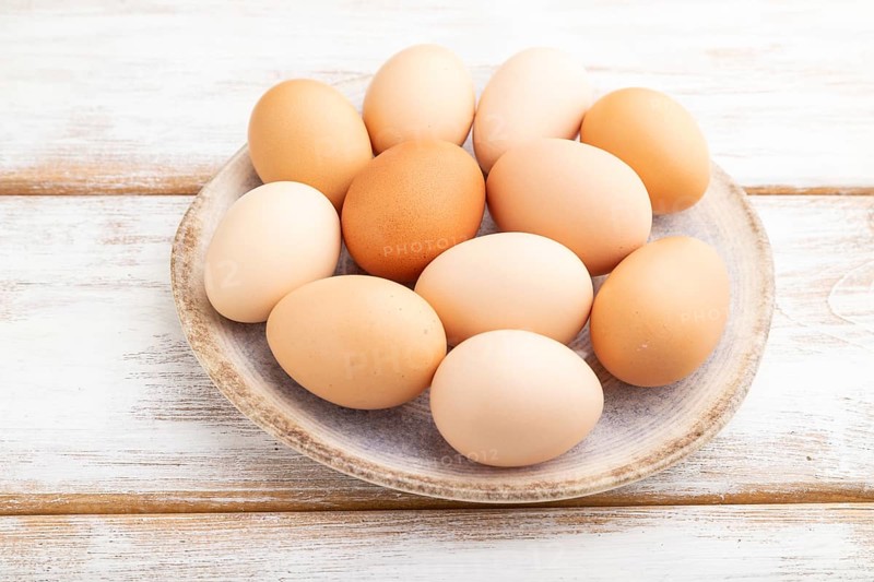 Pile of colored chicken eggs on plate on a white wooden background. side view, close up