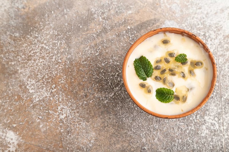 Yoghurt with granadilla and mint in clay bowl on brown concrete background. top view, flat lay, copy space