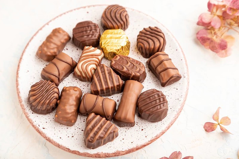 Chocolate candies with cup of coffee and hydrangea flowers on a white concrete background. side view, close up, selective focus