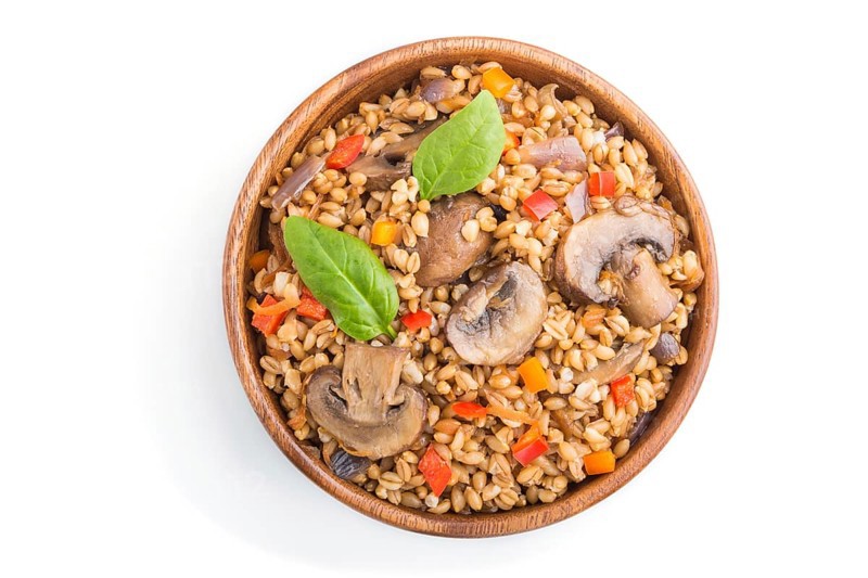 Spelt (dinkel wheat) porridge with vegetables and mushrooms in wooden bowl isolated on white background. Top view, flat lay, close up. Russian traditional cuisine