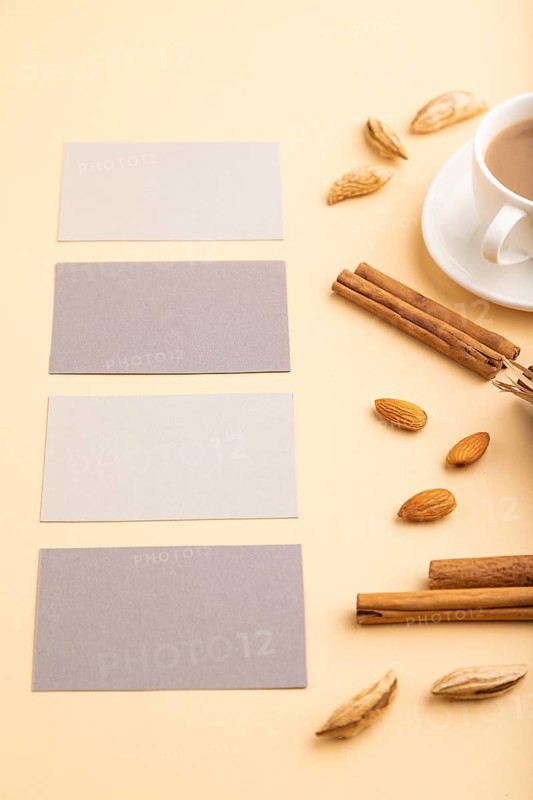 Composition of gray paper business cards, almonds, cinnamon and cup of coffee. mockup on orange background. Blank, side view, still life, copy space
