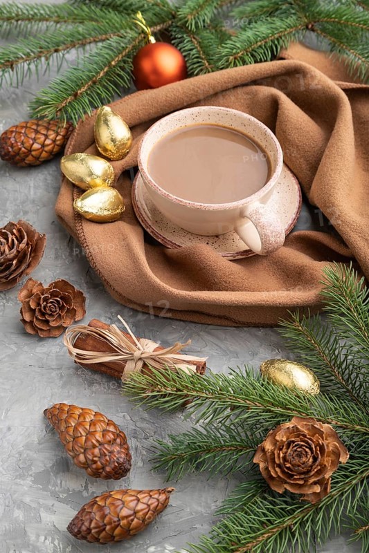 Christmas or New Year composition. Decorations, cones, cinnamon, fir and spruce branches, cup of coffee, wool scarf on a gray concrete background. Side view, close up