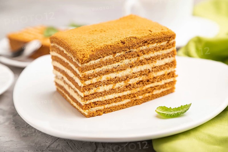 Homemade honey cake with milk cream and mint with cup of coffee on a gray concrete background and green textile. Side view, close up, selective focus