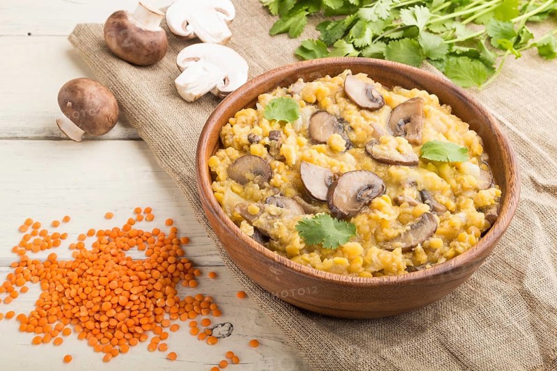 Lentils porridge with champignons and coriander in a wooden bowl on a white wooden background and linen textile. Side view, close up