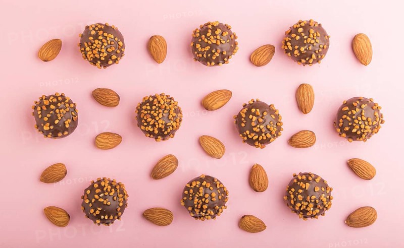 Chocolate caramel ball candies with almonds in a row on a pastel pink background. top view, flat lay