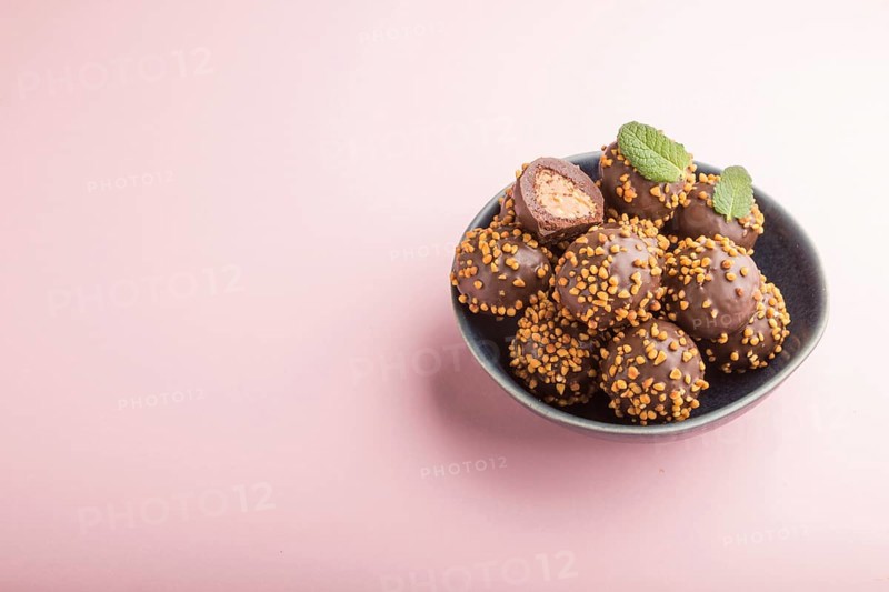 Chocolate caramel ball candies with almonds on a pastel pink background. side view, close up, copy space