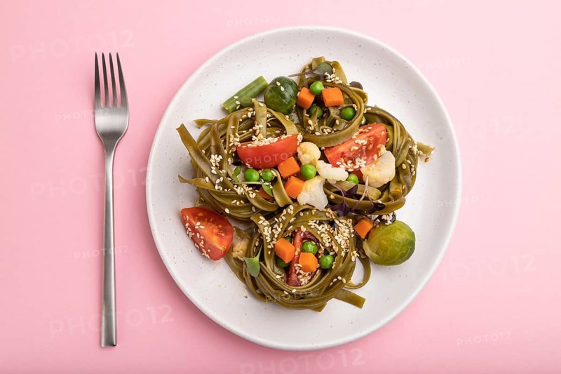 Tagliatelle green spinach pasta with tomato, pea and microgreen sprouts on a pastel pink background. Top view, flat lay, close up