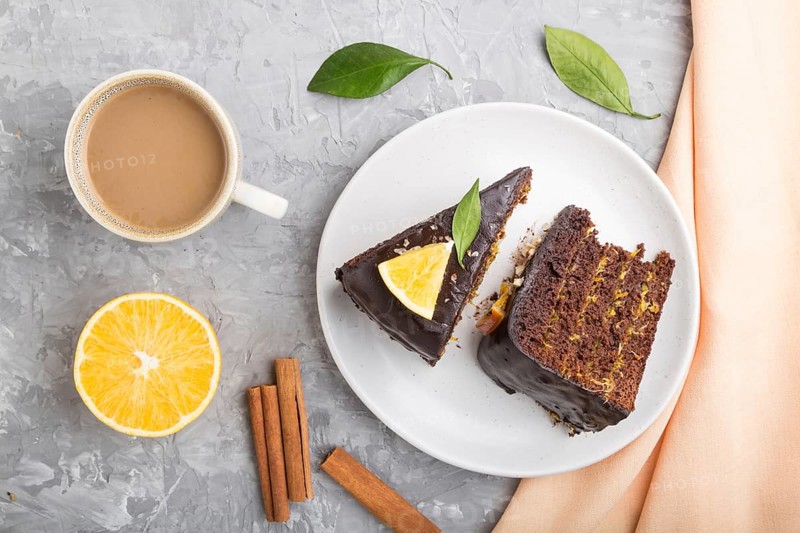 Homemade chocolate cake with orange and cinnamon with cup of coffee on a gray concrete background with orange textile. top view, flat lay, close up