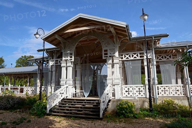 An elegant wooden veranda with white columns and stairs, surrounded by plants under a blue sky, Old railway station Bialowieza Towarowa, built for Russian Tsar Nikolai II, Bialowieza, Podlaskie, Podlaskie, Poland, Europe
