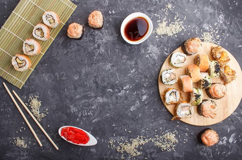 Mixed japanese maki sushi rolls set with chopsticks, ginger, soy sauce, rice on black concrete background. Top view, copy space, flat lay
