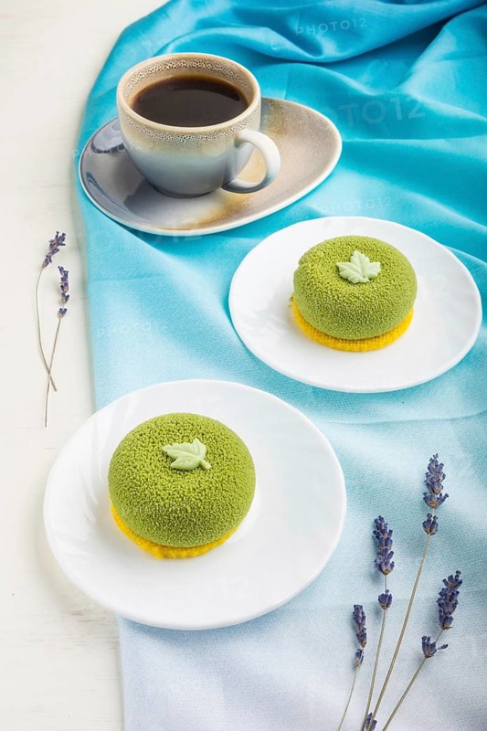 Green mousse cake with pistachio cream and a cup of coffee on a white wooden background and blue textile. side view, close up