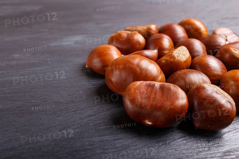 Pile of sweet chestnuts on black wooden background with copy space, top view