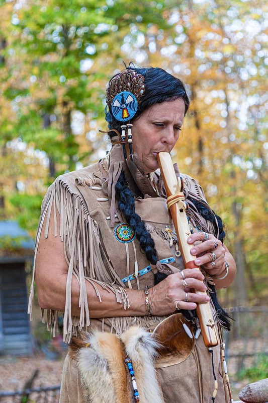Woman dressed as Native American Indian plays hand made wooden flute at Billie Creek Village in Rockville, Indiana, USA, North America