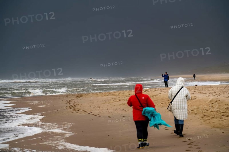 Walkers on the beach, dark storm clouds, choppy sea, autumn on the North Sea in North Holland, between the towns of Egmond aan Zee and Bergen aan Zee, Netherlands