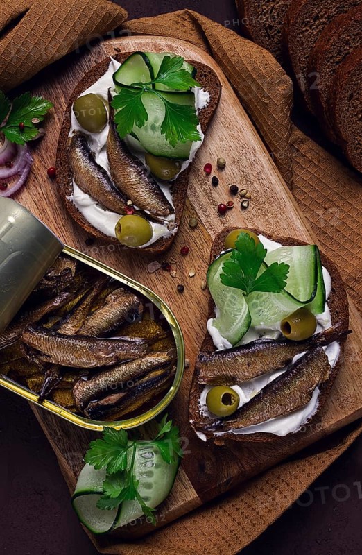 Sandwiches, black bread with sprats, cream cheese, cucumbers, on a cutting board, top view, close-up, no people