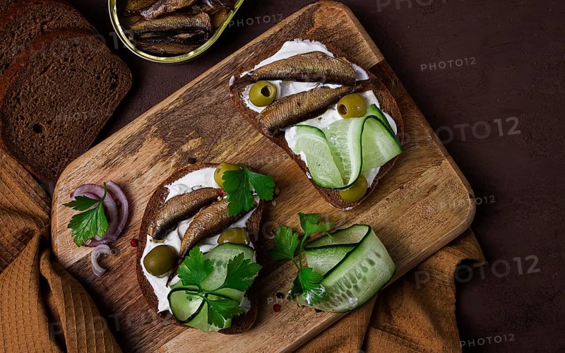 Sandwiches, black bread with sprats, cream cheese, cucumbers, on a cutting board, top view, close-up, no people