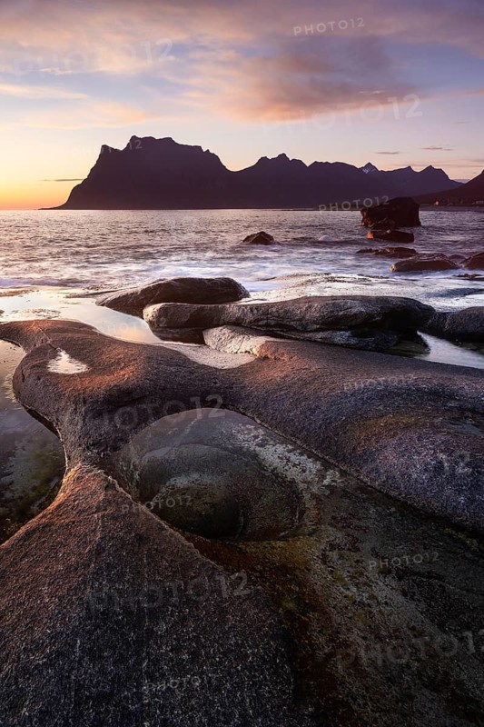 Seascape on the beach at Uttakleiv (Utakleiv), in the foreground stones and the so-called Eye of Uttakleiv. In the background the mountain Hogskolmen. At night at the time of the midnight sun in good weather. Early summer. Uttakleiv, Vestvagoya, Lofoten, Norway, Europe