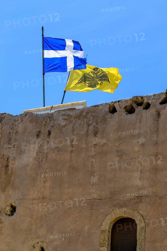 Top left flag of Crete behind it flag with symbol of Eastern Orthodox Greek Orthodox Church yellow background in black black imperial Byzantine double-headed eagle Byzantine Empire of Palaiologian Dynasty insignia of Byzantium with crown sword orb globe on monastery defence tower historic defence tower Xopatera Tower Tower of Xopateras from 19th century of Unesco Site Moni Odigitria Monastery in Festos, Crete, Crete. Unesco Site Orthodox Greek Orthodox Monastery of Moni Odigitria, Festos, Crete, Crete