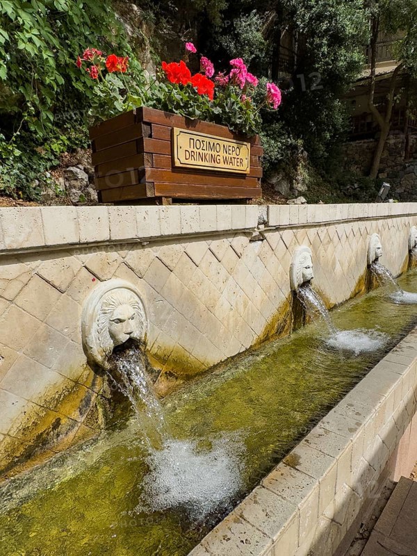 Partial view of lion fountain Venetian fountain Kefalovrisi with 25 waterspouts in the shape of lion's head Lion's head above Plla chain sign Drinking water Drinking water below Catch basin with drinking water on main square of village Spili, Spili, Crete, Greece, Europe