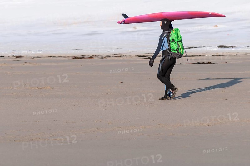 Surfer on the beach of Unnstad with surfboard on her head and green backpack, winter surfing, Lofoten Island Vestvågøya Lofoten, Northern Norway, Norway, Europe