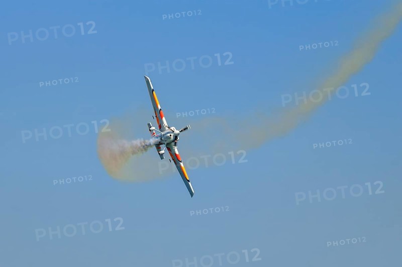 Stunt aerobatic plane performing stunts in blue sky with smoke trail. Concept of speed, difficulty, precision, risk, challenge