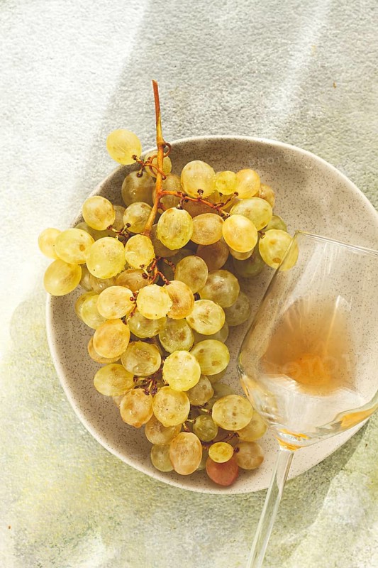 A branch of white grapes, on a gray plate, with a glass of white wine, top view, natural light, food concept, no people
