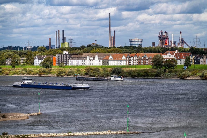 Cargo ship on the Rhine near Duisburg-Laar, houses on Deichstraße, industrial backdrop of the ThyssenKrupp Steel steelworks in Bruckhausen, North Rhine-Westphalia, Germany, Europe