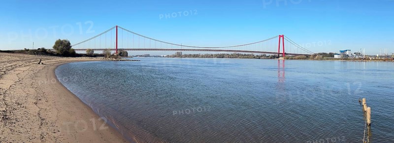 Panorama view from the left bank of the Rhine, western bank of the Rhine, of an earth-anchored suspension bridge with two abutments and red steel piers nicknamed the Golden Gate of the Lower Rhine over the River Rhine, with a total length of 1228 metres the longest suspension bridge in Germany, Emmerich, North Rhine-Westphalia, Germany, Europe