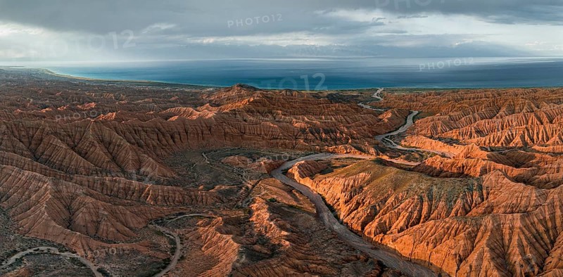 Riverbed runs through a landscape of eroded hills, badlands at sunset, Issyk Kul Lake in the background, aerial view, Canyon of the Forgotten Rivers, Issyk Kul, Kyrgyzstan, Asia