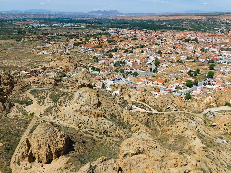 Expansive view of a village surrounded by hilly, rocky landscapes under a clear sky, aerial view, cave dwellings, cave neighbourhood, Troglodytos, Guadix, Granada, Andalusia, Spain, Europe