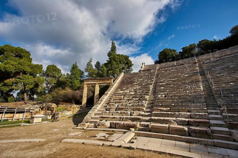 Partially restored amphitheatre under a blue sky next to green vegetation, Ancient Amphitheatre, Epidaurus, Peloponnese, Greece, Europe