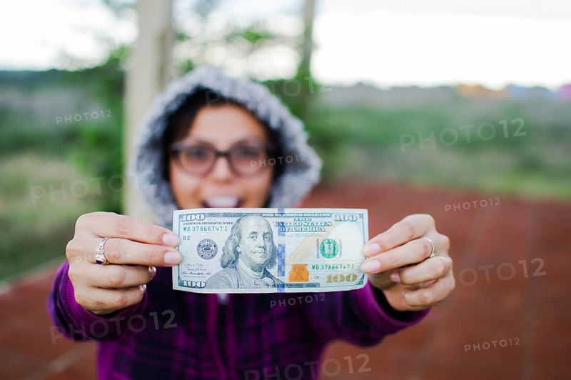 Amazed woman showing 100 dollar bill outdoors