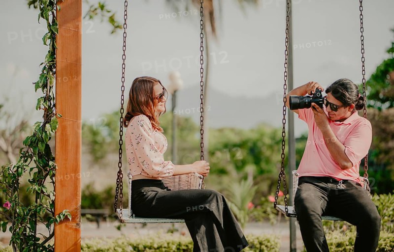 Boyfriend taking a photo of his girlfriend on a swing in a park. Boyfriend photographing girlfriend sitting on a swing