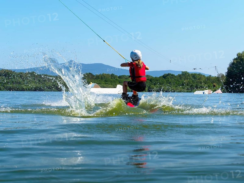 Boy or girl, jump over jump with wakeboard, red life jacket and water sports, water skiing in wakepark, Stráž pod Ralskem, Czech Republic, Europe
