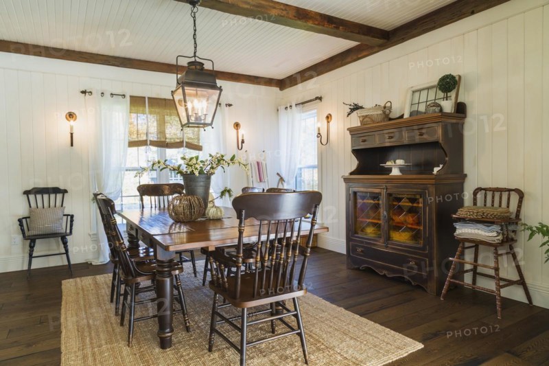 Brown stained pine wood antique reproduction style dining table with high back chairs in dining room with rug and dark brown larch wood floorboards inside country style home, Quebec, Canada, North America