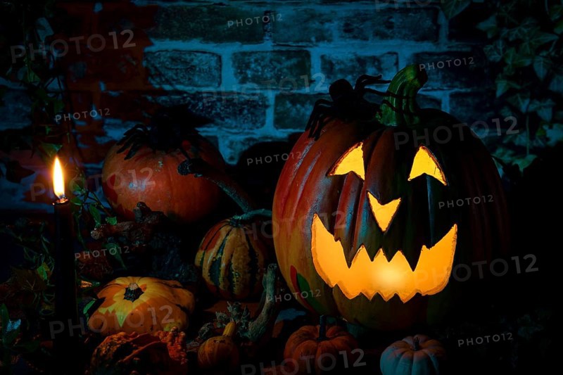 Glowing Halloween pumpkin, surrounded by a candle and various decorative pumpkins