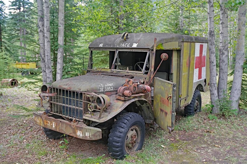 Rusty, old army ambulance, with Red Cross symbol between trees in the forest, former army camp, Yukon Territory, Alaska Highway, Discovery Lodge, Yukon Territory, Canada, North America