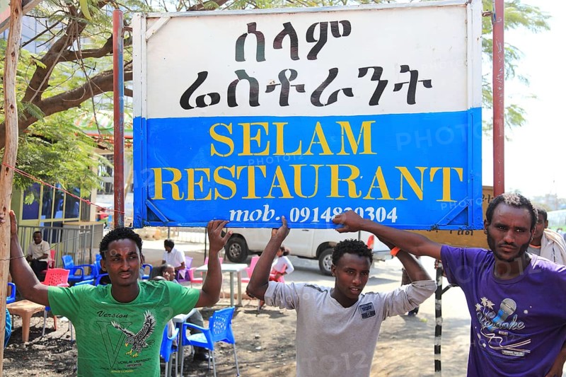 In a village in the highlands between Mekele and Lalibela, advertising sign for a restaurant, young men in front of it, Ethiopia, Africa