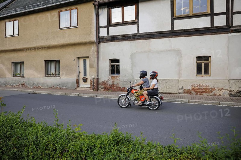 Symbolic photo on the subject of youth in the East. A boy and a girl ride a Simson moped past old houses along a village street in Ziegenrück, 20/07/2024