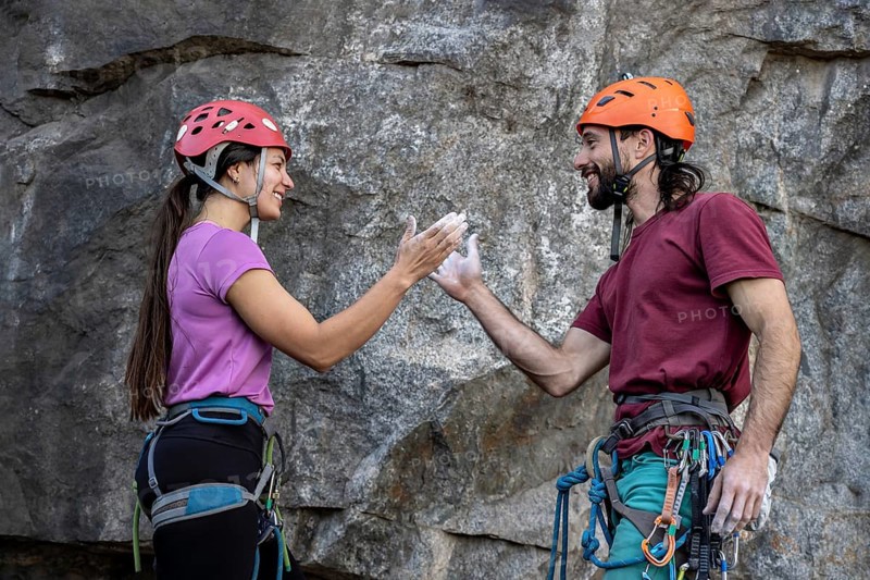 A climber gives a high five to his female partner while climbing a rocky wall. They show teamwork, encouragement, and adventure in an outdoor climbing setting